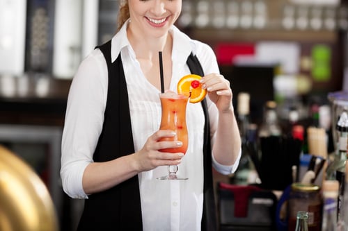 Female bartender making a tropical fruit cocktail holding an elegant long glass of beverage in her hand as she adds the sliced orange garnish to the rim