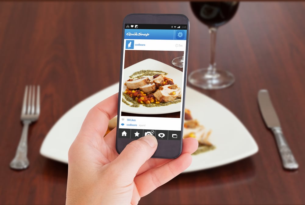Female hand holding a smartphone against high angle view of delicious chicken dish with salsa